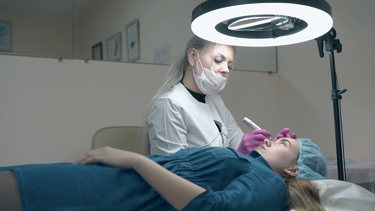 una esteticista experta colorea las cejas en negro con una pistola de tatuaje