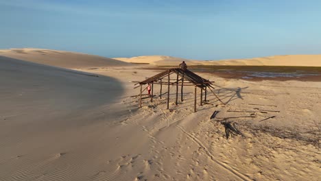 men work on wooden shelter frame amid sand dunes near parnaíba river in araioses, maranhão, brazil. aerial orbiting