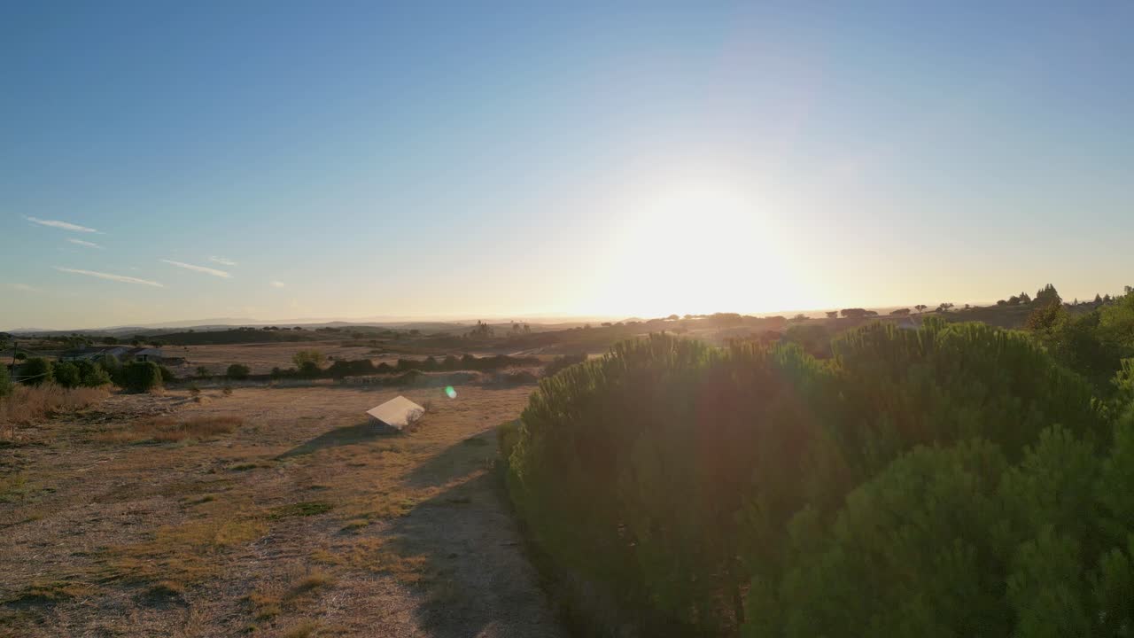 aerial view rises from below, capturing the sun peeking through the trees, illuminating the landscape with warm golden light.