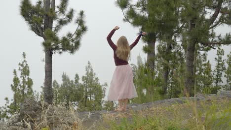 joyful blonde haired woman in long pink skirt black top swings arms happy and barefoot, rear view