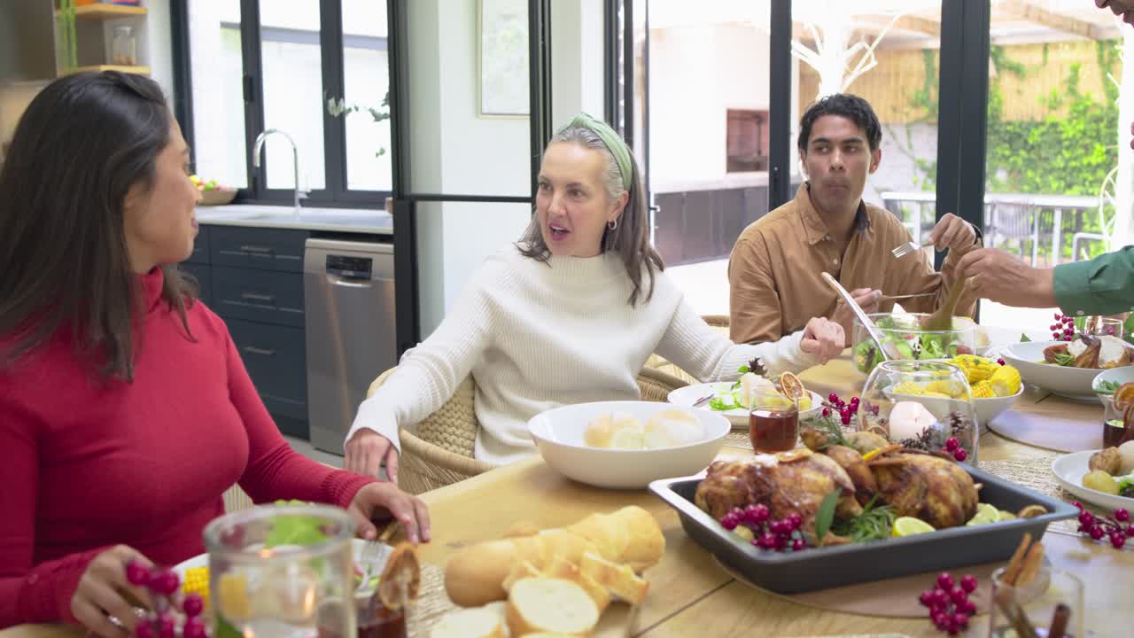 Diverse family sharing dinner with man spooning roast chicken at home dining table, tasting salad