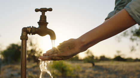 mujer lavando las manos bajo el grifo con agua dulce en tierras de cultivo rurales al amanecer