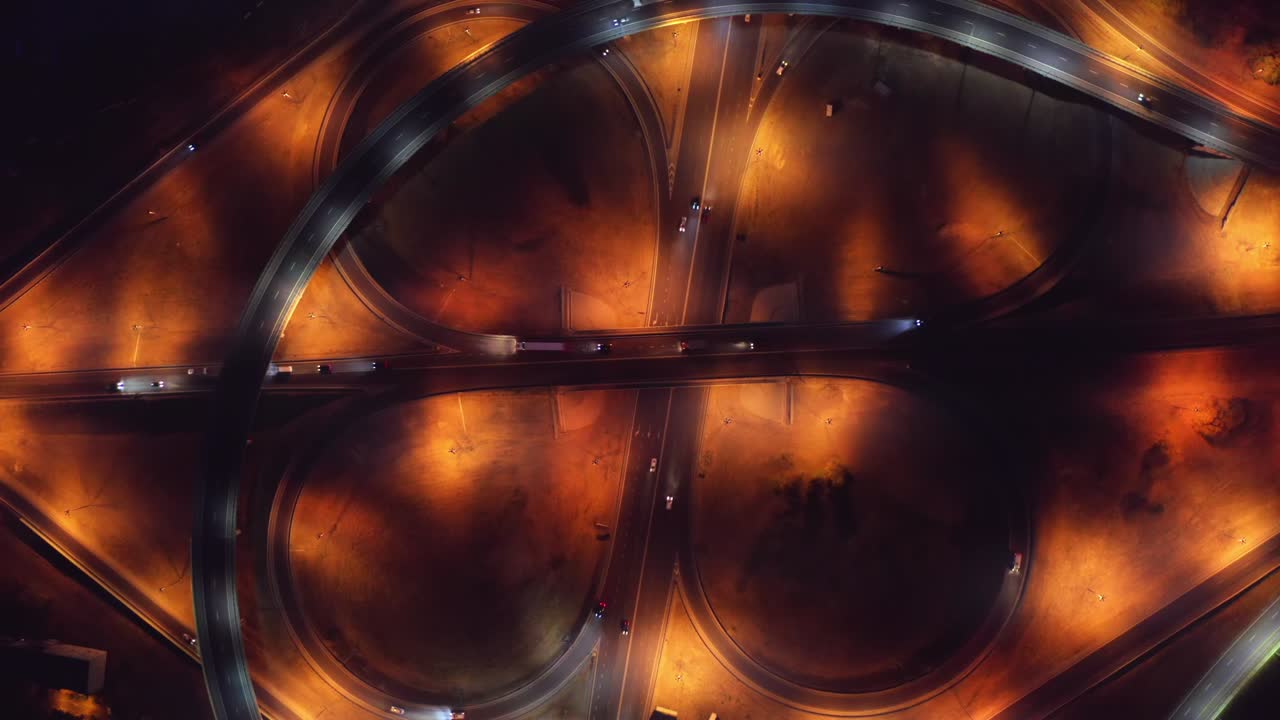 Road intersection, bridges, highways and car traffic in blurred speed motion, aerial top view at night
