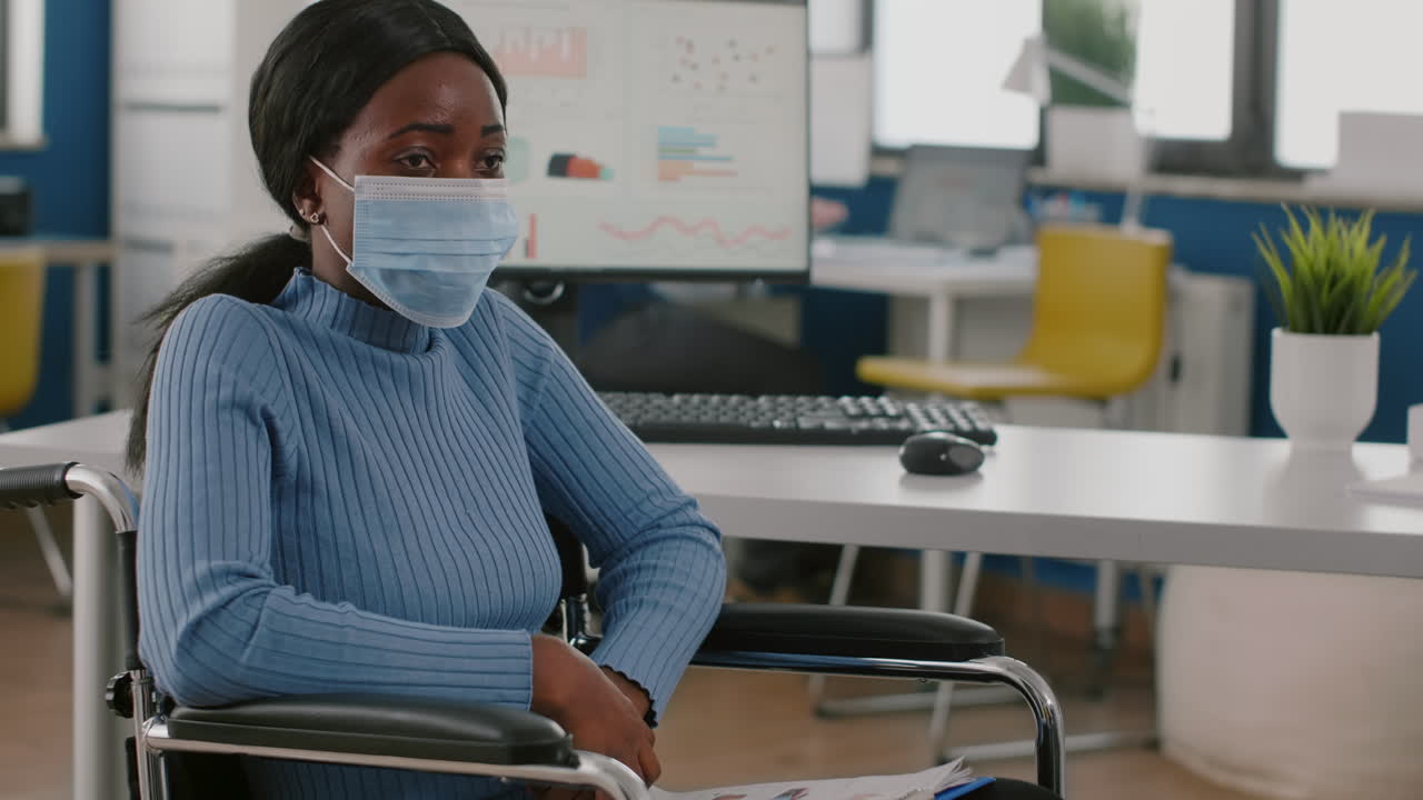 Donna africana immobilizzata in sedia a rotelle che sembra persa nel nuovo ufficio normale