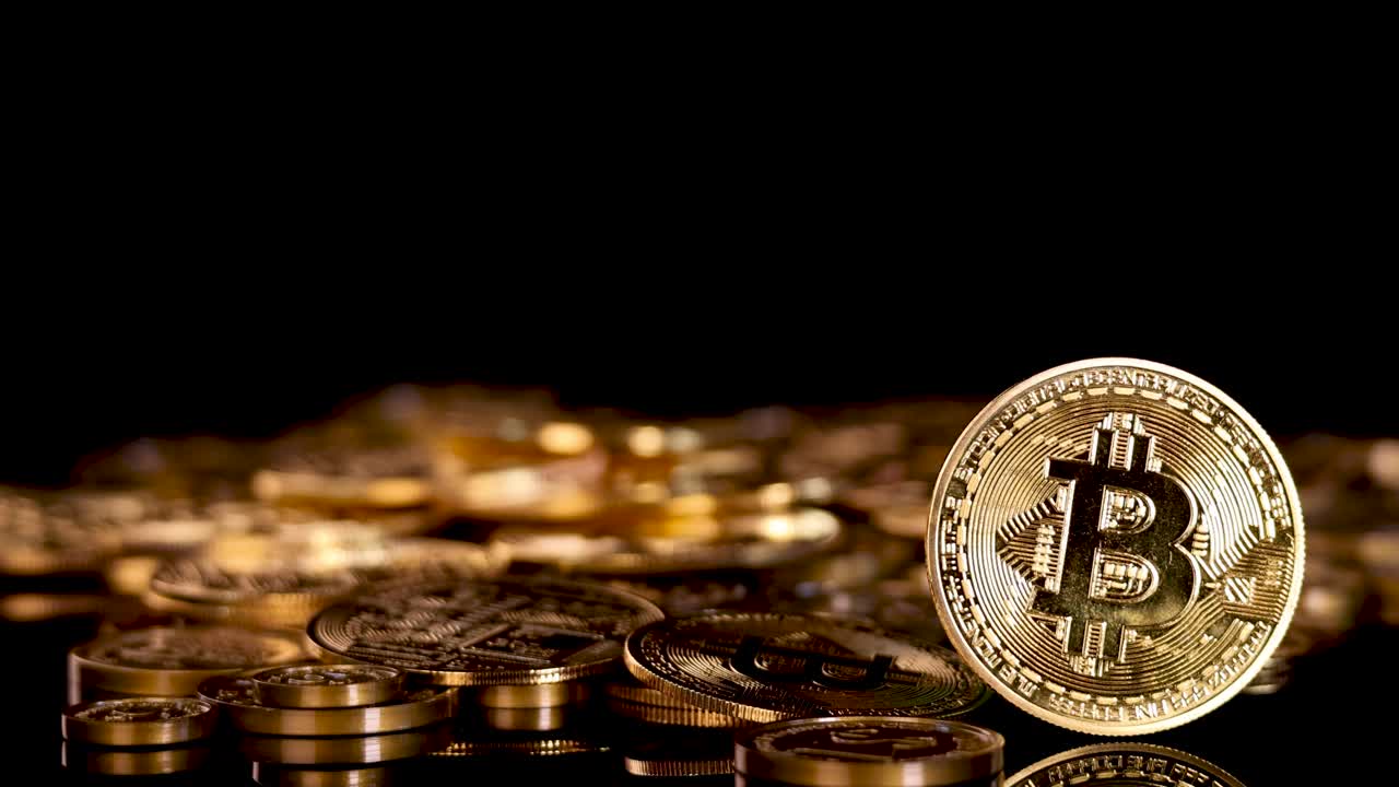 Hand drops gold Bitcoin coin onto pile of coins, dramatic lighting, close-up, black background