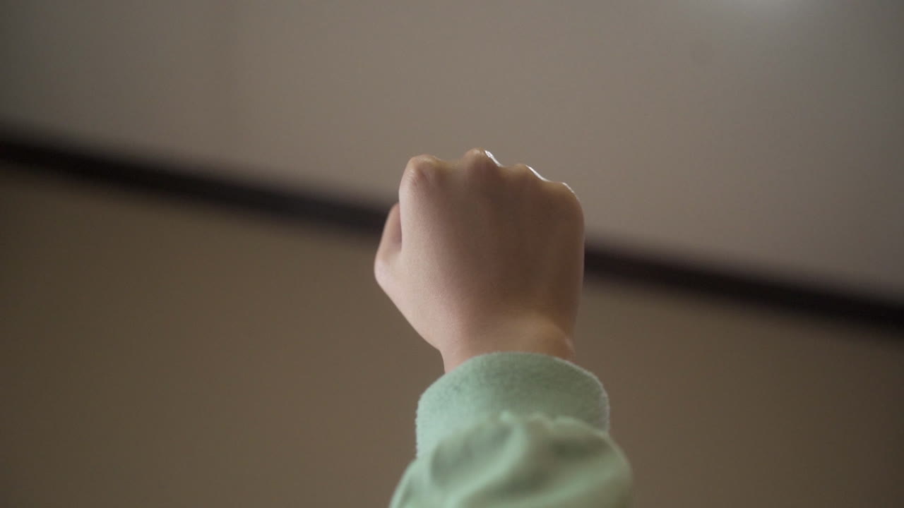 Close Up Of Female Hand In Fist Opening With Forearm Upward Against Blurry Background.