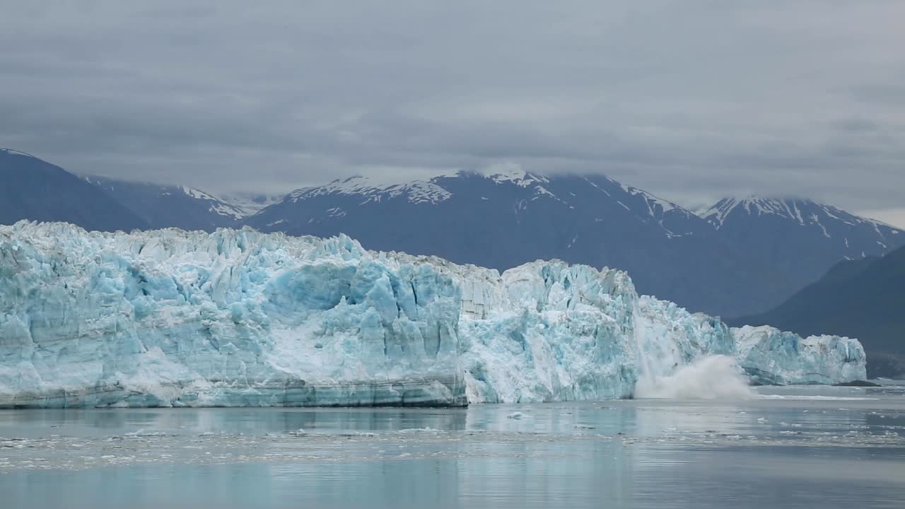 imágenes del calentamiento del cambio climático global: un trozo de glaciar se derrite, se desprende y se cae en alaska en un día oscuro y sombrío con montañas cubiertas de nieve en el fondo