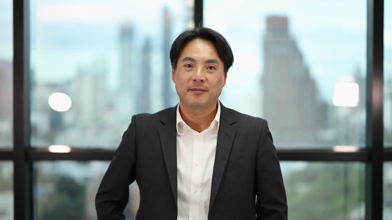 Confident Asian businessman contemplates, then smiles with raised finger in bright, contemporary office setting