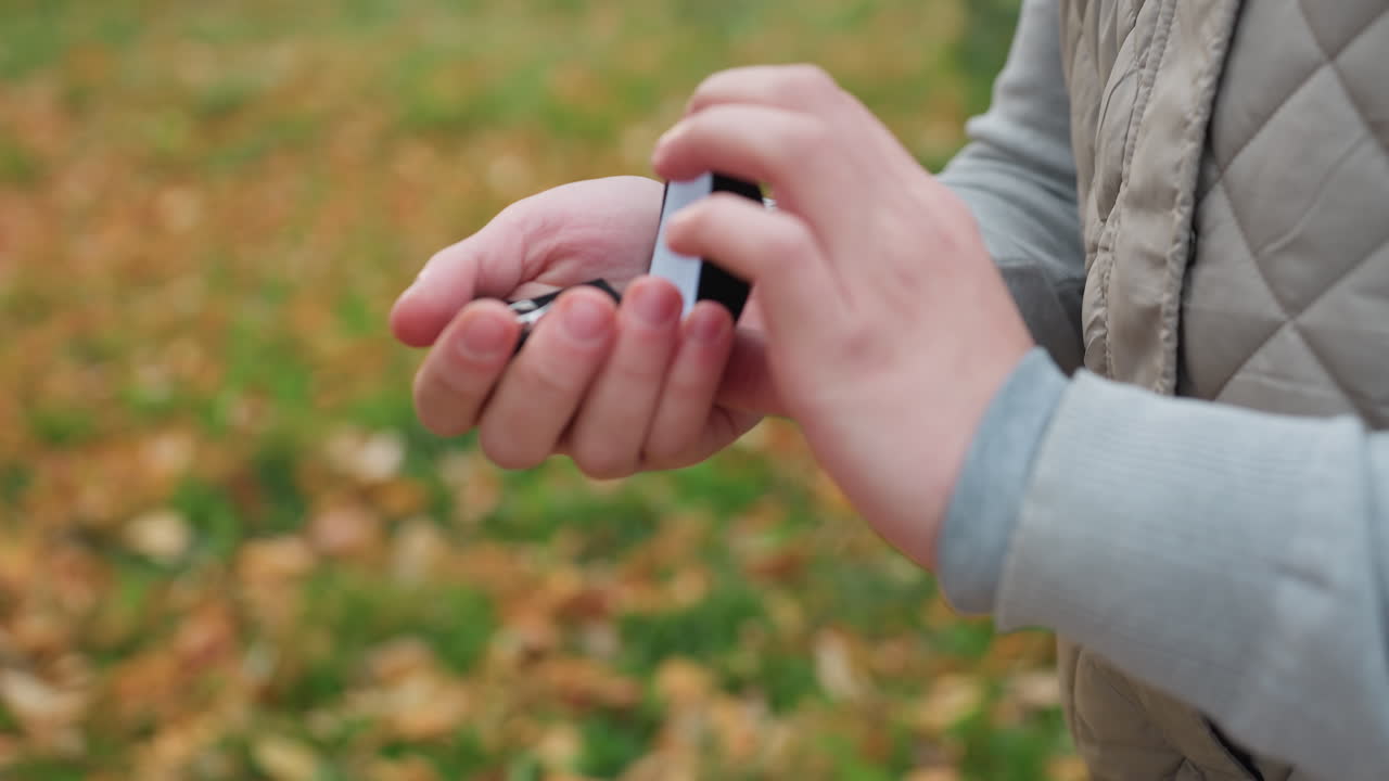 Close up of man preparing to propose on one knee holding ring with both hands while wearing quilted jacket in soft autumn setting with colorful blurred background of grass and fallen leaves