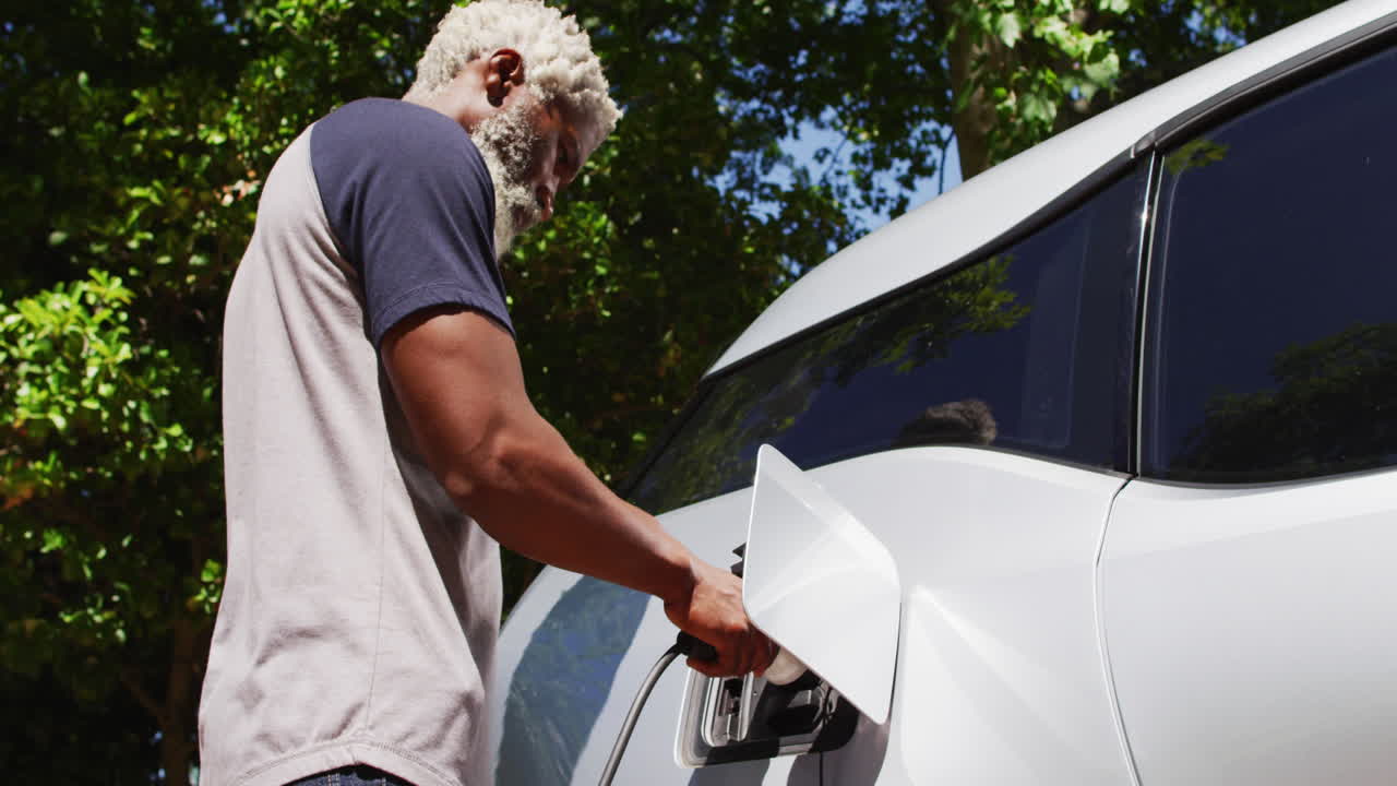 hombre mayor afroamericano cargando un coche eléctrico en un día soleado