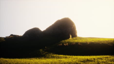 sunset over a grassy field with a large rock in the foreground