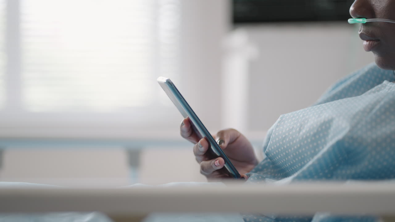 una mujer joven escribe un mensaje en su teléfono mientras está acostada en una sala de hospital. una niña africana está acostada en una sala conectada a dispositivos de ecg y oxígeno en una máscara y escribe mensajes a familiares