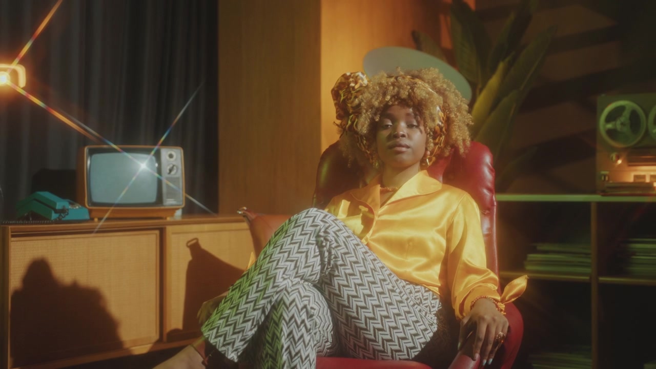 Stylish Black Woman Sitting in Chair and Posing with Confidence in Retro Studio