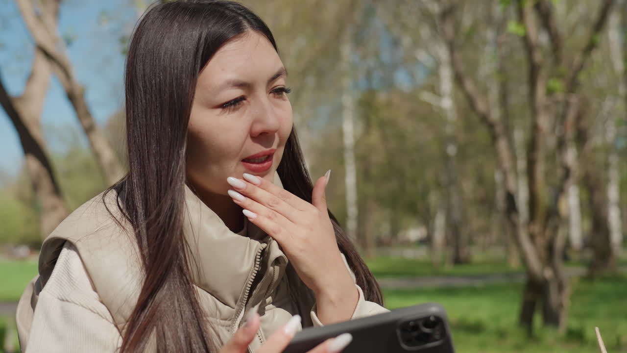 여성이 장치를 공개해요. 젊은 여성이 자연 속에서 최신 기술을 발견하고 신나서 공개하며, 한 여성이 꽃이 피는 봄 나무와 햇살 속에서 콤팩트한 전자 장치를 즐겁게 선보입니다.