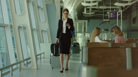 bonita mujer de negocios con anteojos caminando por el pasillo del aeropuerto con un teléfono inteligente en las manos y luego sentada en el banco