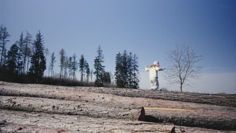 Blonde-girl-in-pink-hat-balancing-on-logs-in-a-sunny-meadow