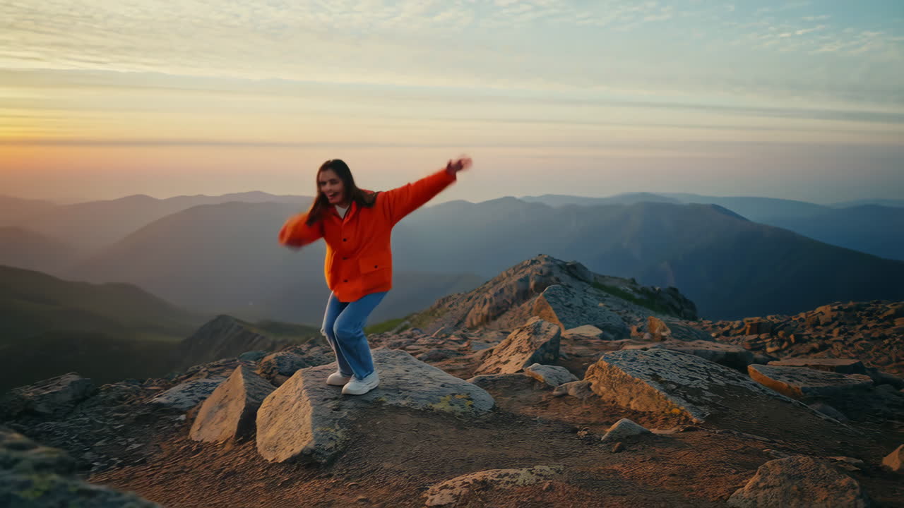 Young woman enjoying freedom and balancing on a mountain peak at sunset