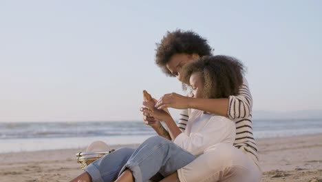 loving mother and daughter having picnic at seashore and eating croissants