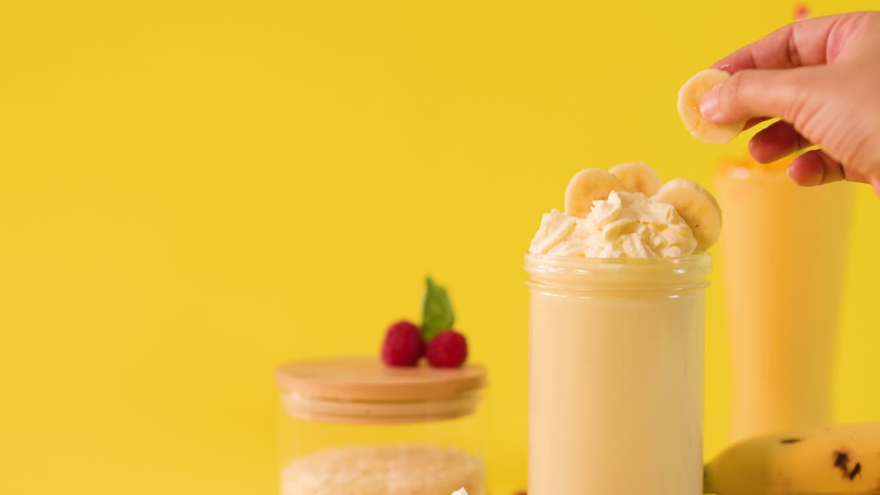 Human hand adds banana slices onto whipped cream banana smoothie in bright studio lighting