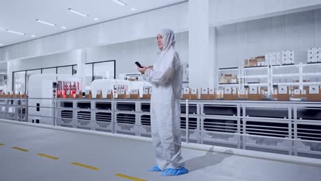 full body side view of asian male scientist using smartphone and look around while standing with conveyor for packaging coffee beans in bags at coffee factory