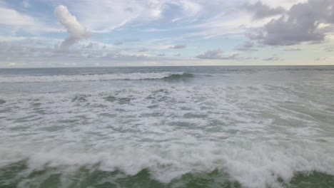 Aerial-truck-right-of-foamy-sea-waves-hitting-the-coast-on-a-cloudy-day-in-Dominicalito-Beach,-Costa-Rica