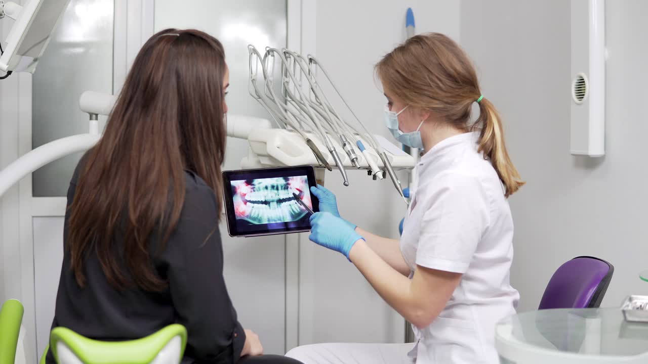 un dentista femminile sta mostrando i denti a raggi x su un tablet a una giovane paziente femminile. il dentista indossa un camice da laboratorio