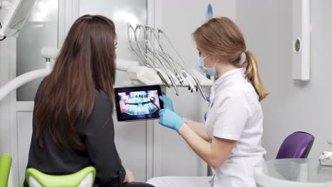 el dentista está mostrando dientes de rayos x en una tableta a una joven paciente. el dentista está usando una bata de laboratorio