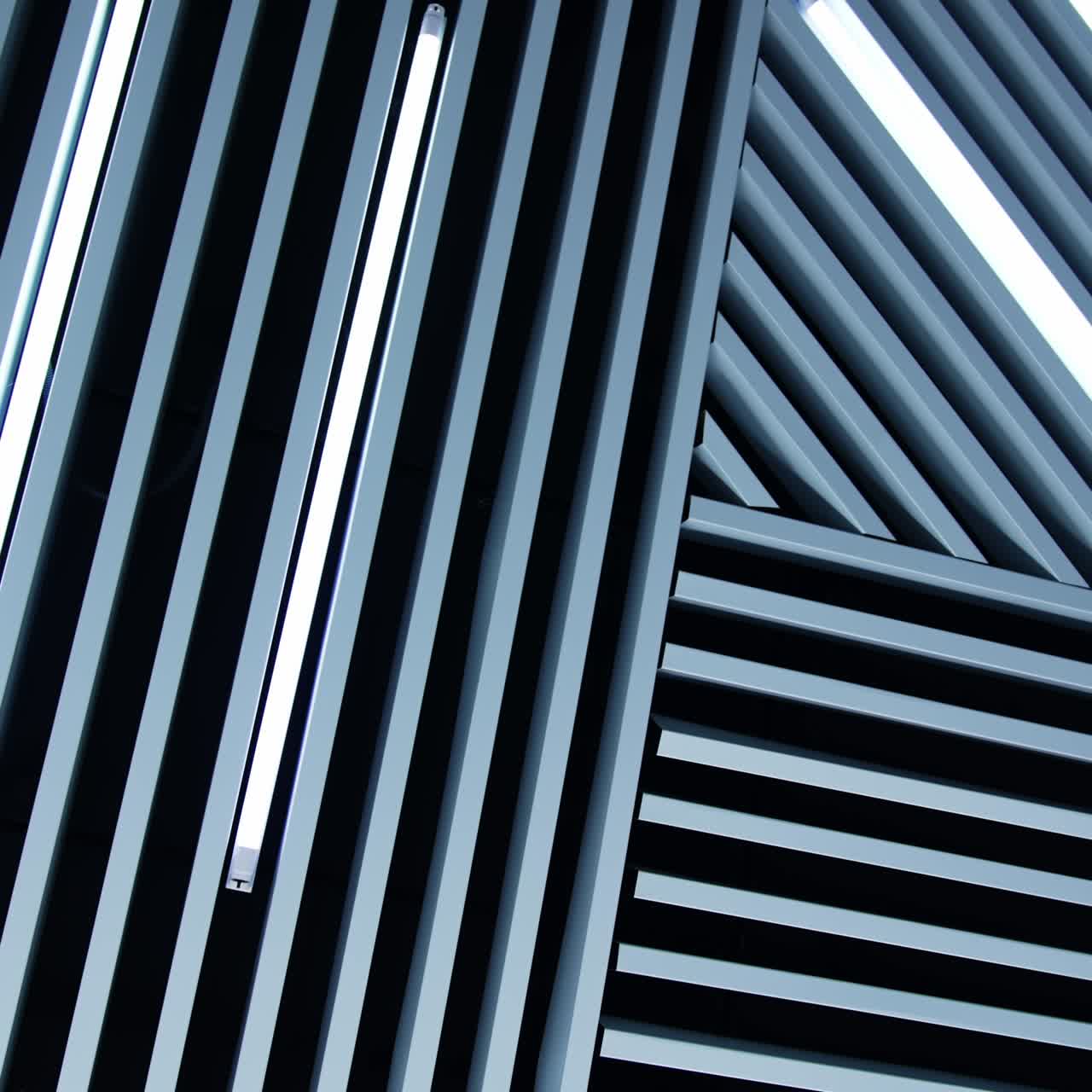 Unusual design of the ceiling in the room. Decorative planks with lamps of daylight among them. Low angle view
