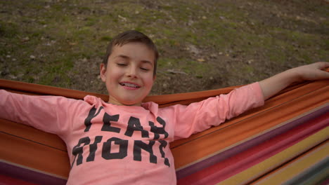 frontal portrait of teenage boy smiling in swinging hammock in forest.