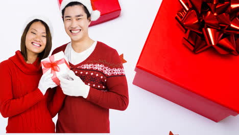composition of asian couple in santa hats holding christmas present on white background with boxes
