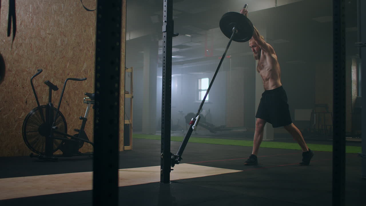 체육관 에서 운동 하는 남성 전투자 가 한 무 ⁇  에 서서 손 으로 지뢰 바 를 밀고 있다