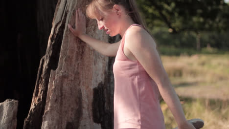 a young woman holds the tree while stretching her leg with her hand before jogging or running in the park on a sunny day