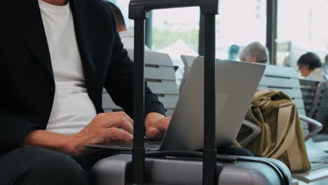 businessman uses laptop, waiting for a flight in airport terminal or train station, traveling entrepreneur working online on computer sitting in a boarding lounge of airline hub with airplanes