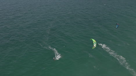 aerial: kite surfers ride in opposite directions on choppy green sea
