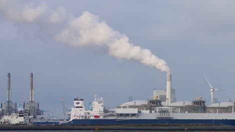 large commercial ship in dock with chimney emitting steam or smoke in the background