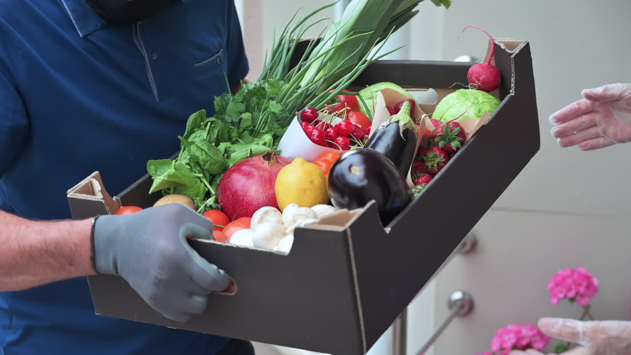 Woman receiving a box of fresh fruits and vegetables from a masked delivery man