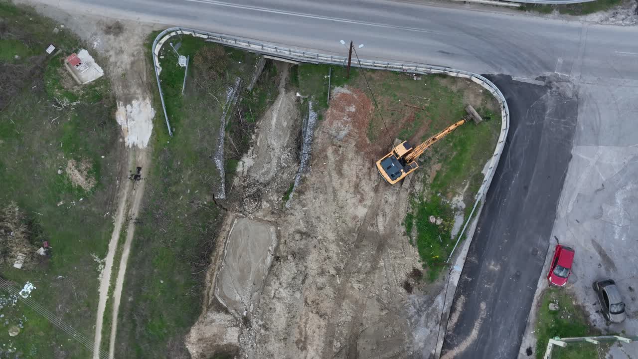 Aerial drone ascending and twisting over excavator working on construction site.