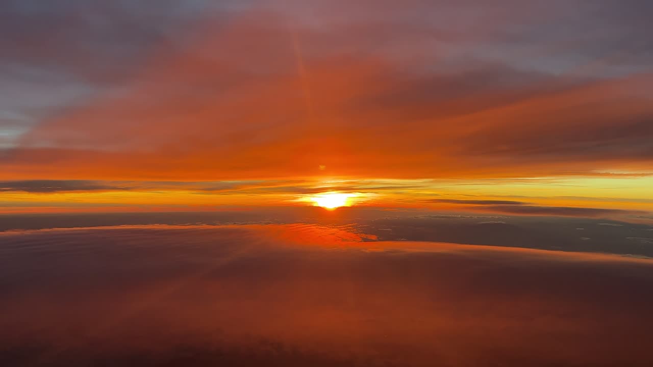 An aerial view of a sunset while flying at the upper atmosphere between layers of golden ethereal clouds. Footage taken from a jet cockpit. handheld camera shot