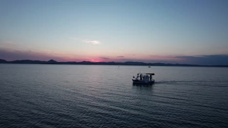 Side-view-tracking-follows-dive-boat-heading-out-to-ocean-at-dawn,-pink-hue-on-horizon