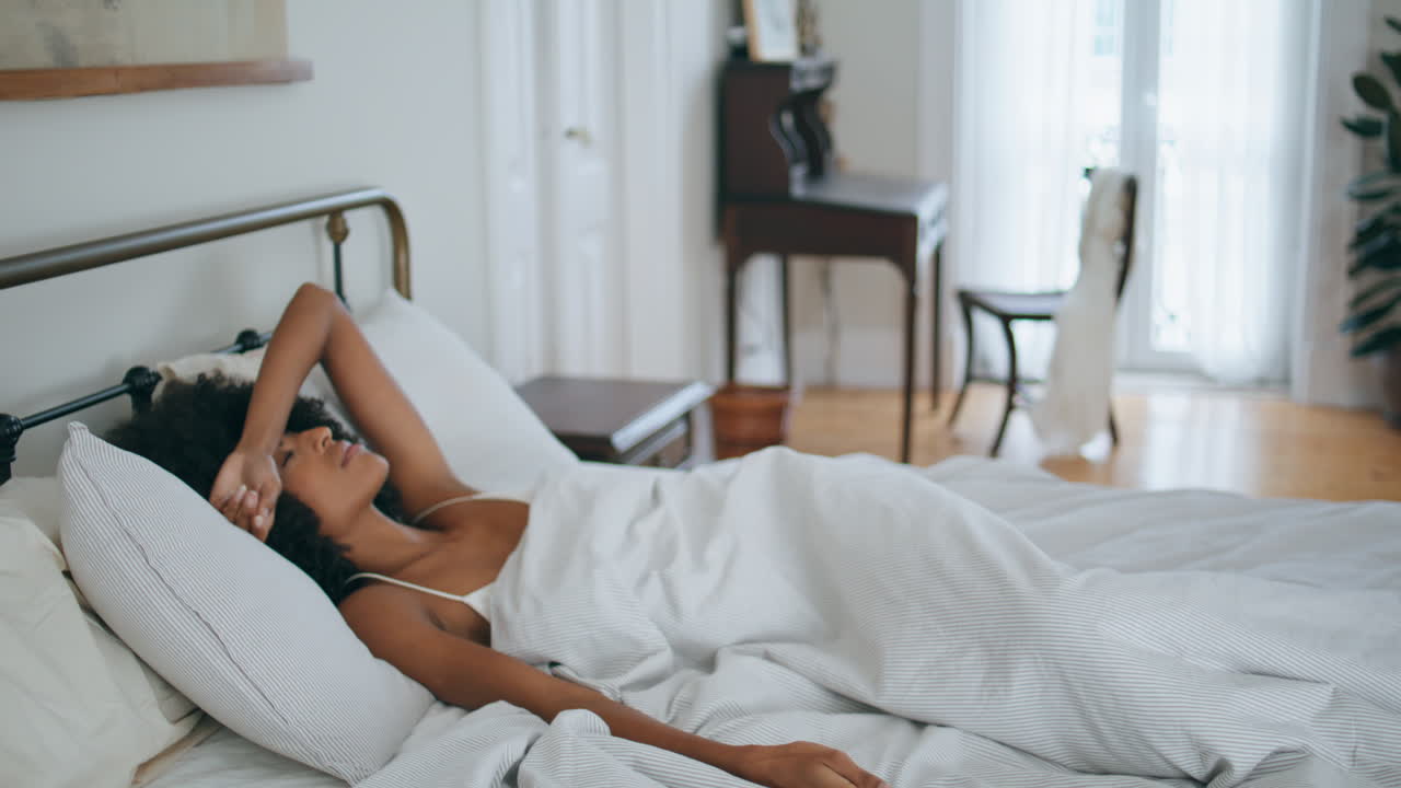 Modella assonnata che si abbandona sul cuscino al mattino presto. Una donna dai capelli neri è sveglia dopo l'insonnia.