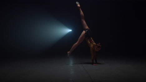 Athletic-woman-doing-handstand-in-dark-studio.-Flexible-gymnast-training-indoors