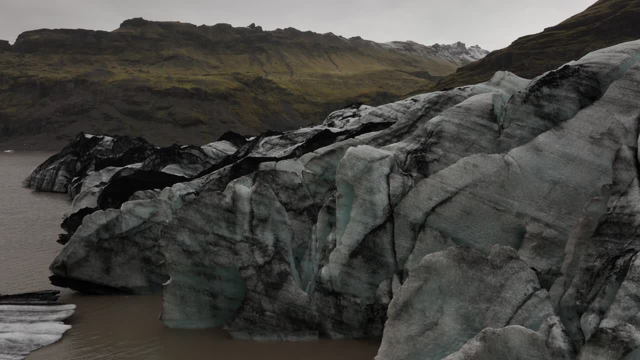 Detailed view of the jagged ice formations at the edge of Sólheimajökull glacier meeting a glacial lagoon in Iceland, with mountainous terrain in the background.