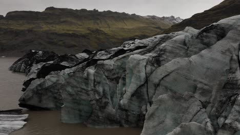 detailed view of the jagged ice formations at the edge of sólheimajökull glacier meeting a glacial lagoon in iceland, with mountainous terrain in the background.