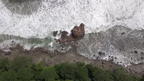 Toma-Aérea-A-Vista-De-Pájaro-De-Las-Olas-Del-Océano-Chocando-Contra-Las-Rocas-En-La-Orilla