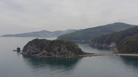 costa marina con acantilados insulares con árboles verdes a los lados en un día nublado con instalaciones portuarias a gran distancia