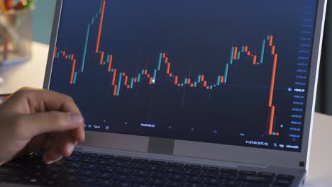 male closely following stock market and cryptocurrency charts on laptop.