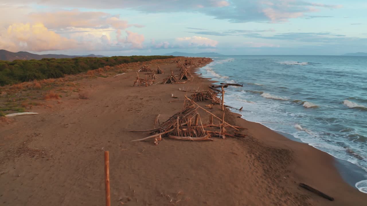 съемка с беспилотника с воздуха соснового леса и песчаного пляжа на берегу моря в культовом природном парке маремма в тоскане, италия, с драматическим облачным небом на закате, и деревянными типи вдоль пустого пляжа