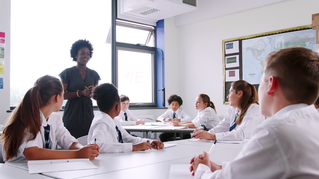 tutora de escuela secundaria grupo de enseñanza de estudiantes vestidos con uniforme trabajando alrededor de mesas en el aula