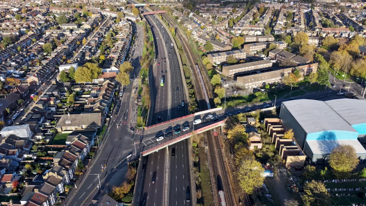 Drone hyperlapse over A12 in Leytonstone, London, along road and Central Line train track, with cemetary to right. Cars and trains move below, with large cloud shadows drifting across the landscape