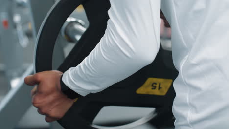rear close up of gym attendant returning weight plate into iron barbell rack on rubber flooring, showcasing hands guiding heavy plate into position during post workout equipment cleanup